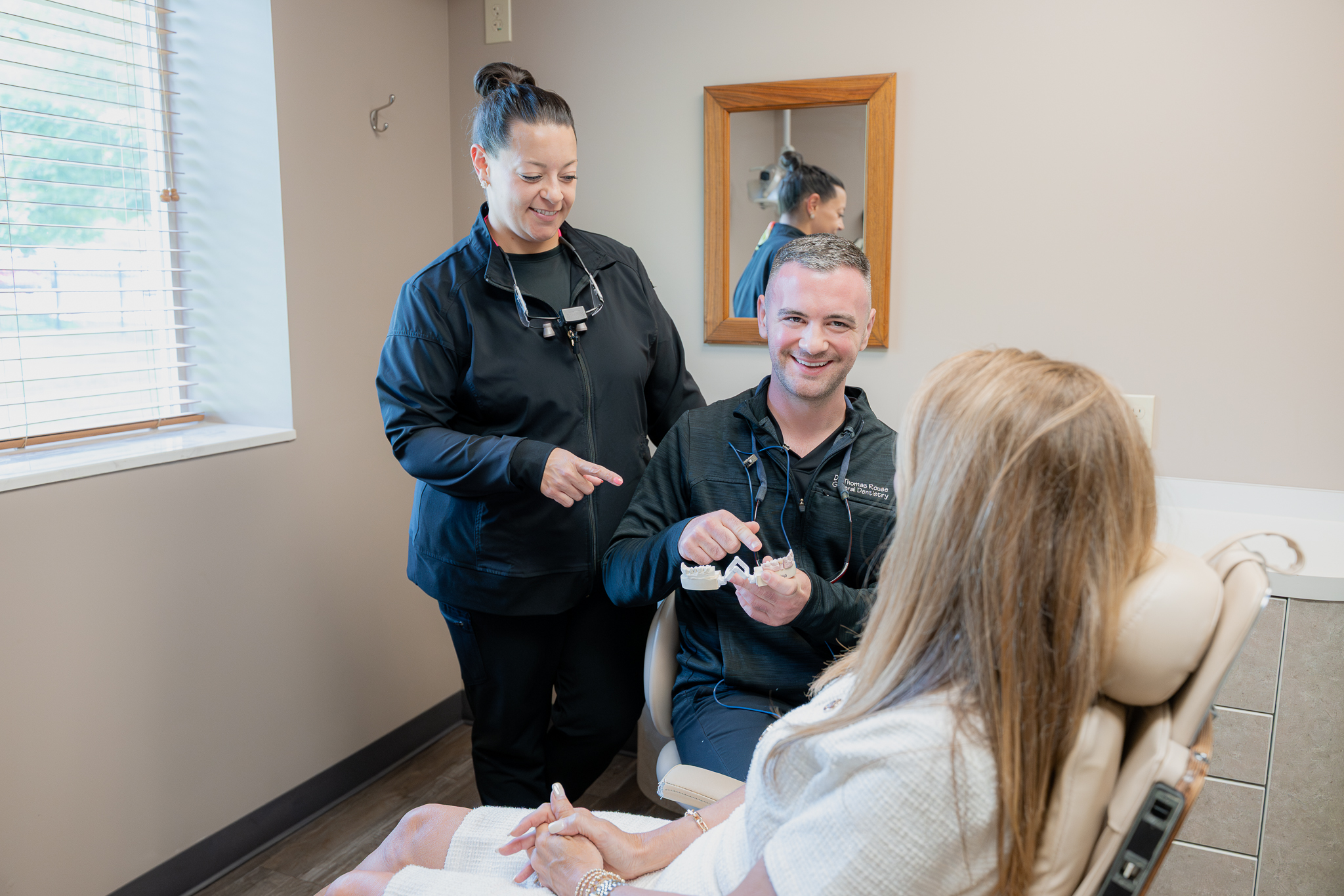 Dr. Thomas Rouse showing a patient a dental model as an assistant looks on