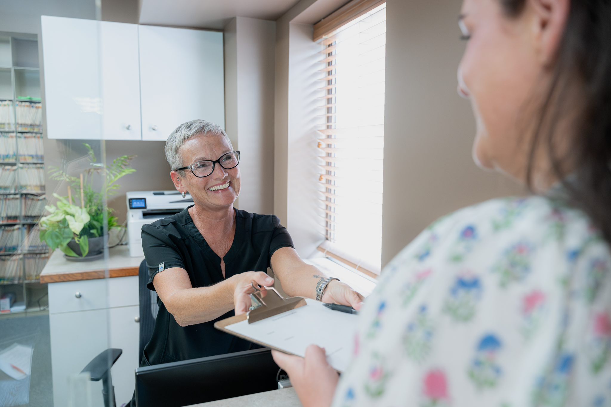 Smiling front desk team member handing a clipboard to a patient