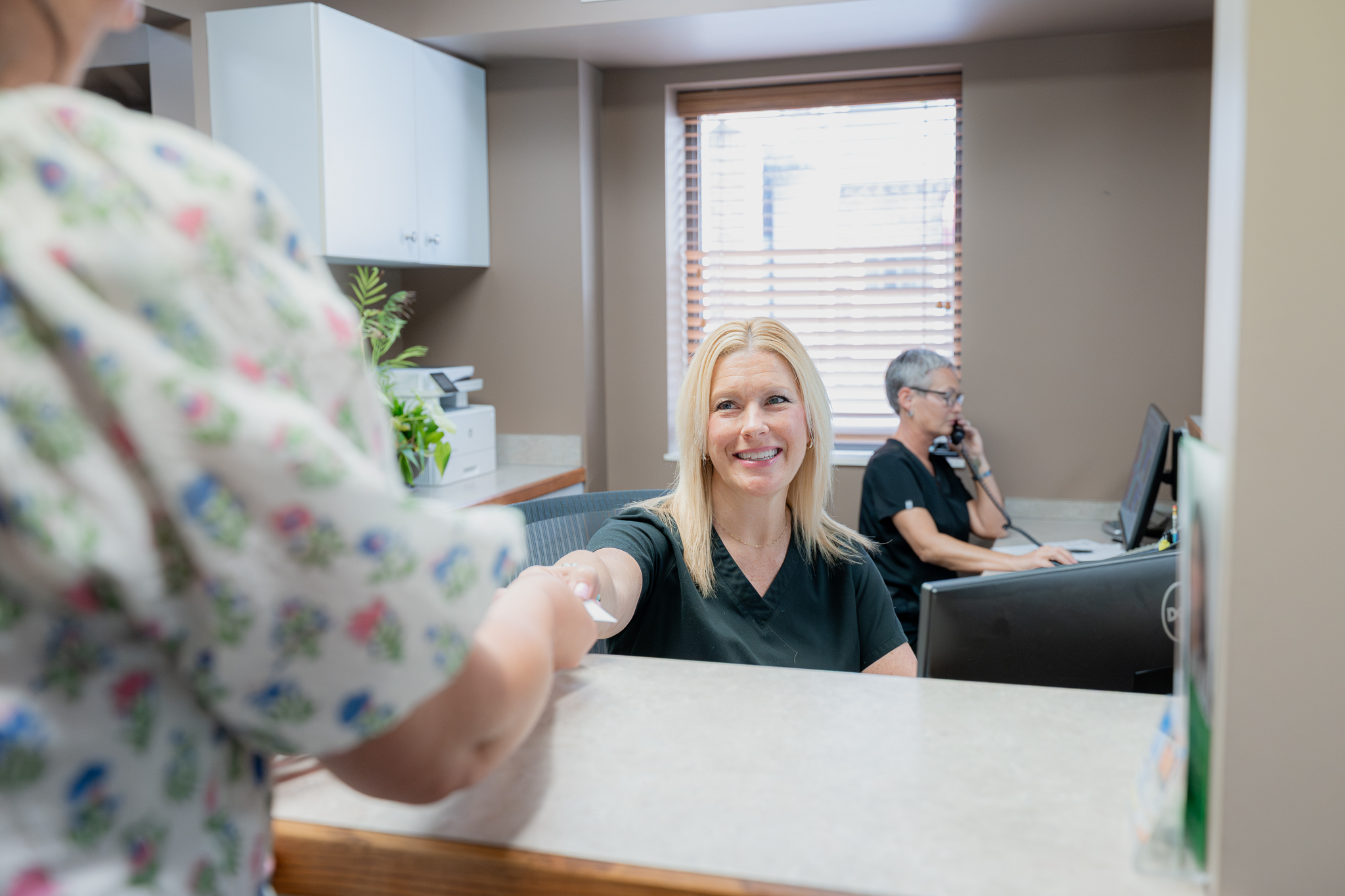 Front desk team member greeting a patient as a colleague takes a phone call