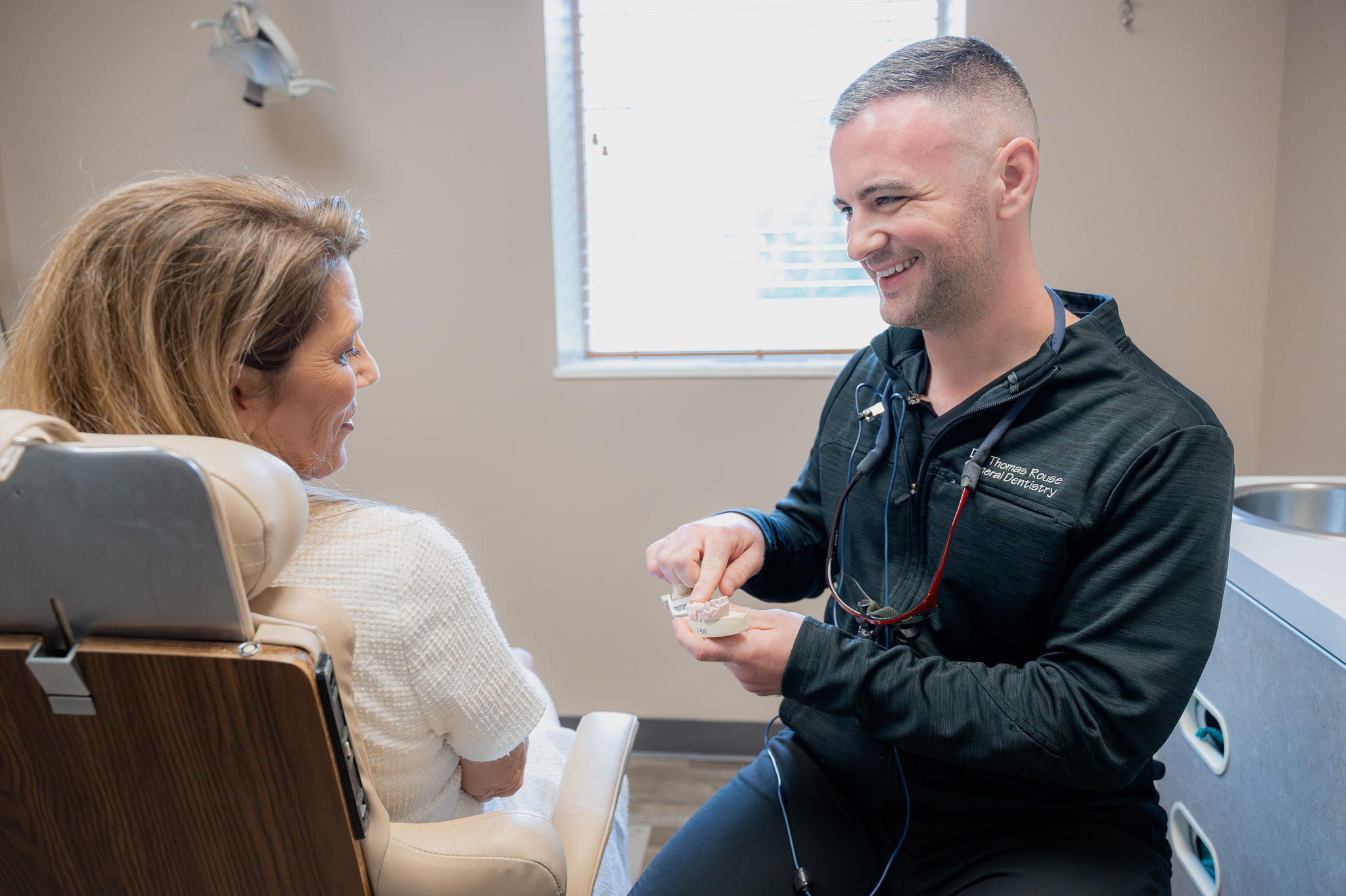 Dentist smiling as he shows a seated patient a dental model