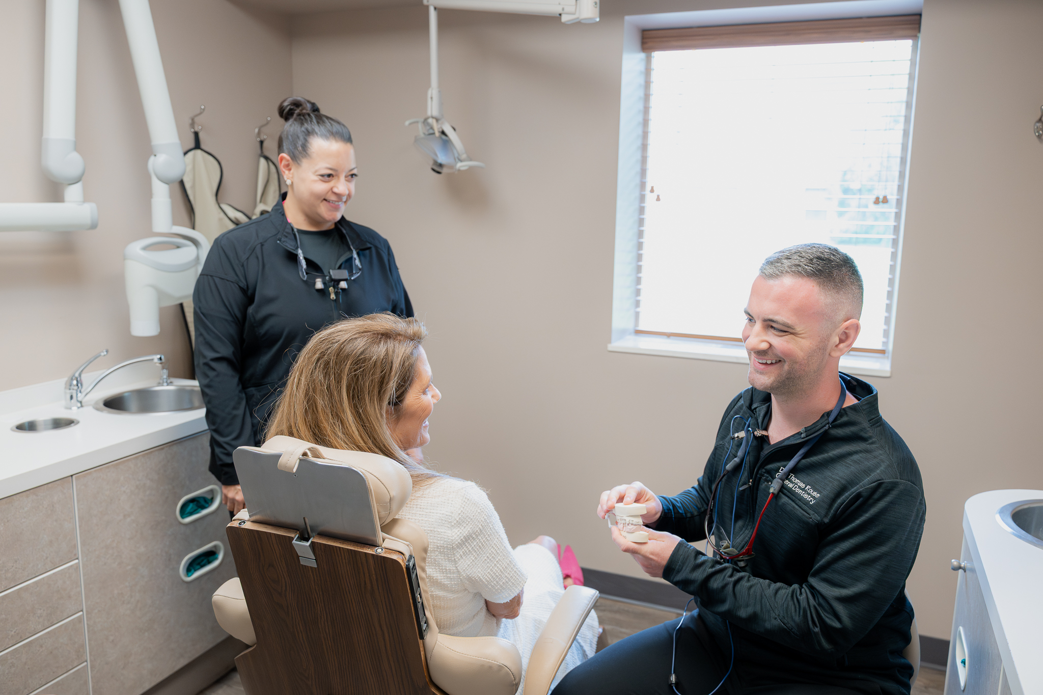 Dentist explaining a dental model to a patient as an assistant looks on