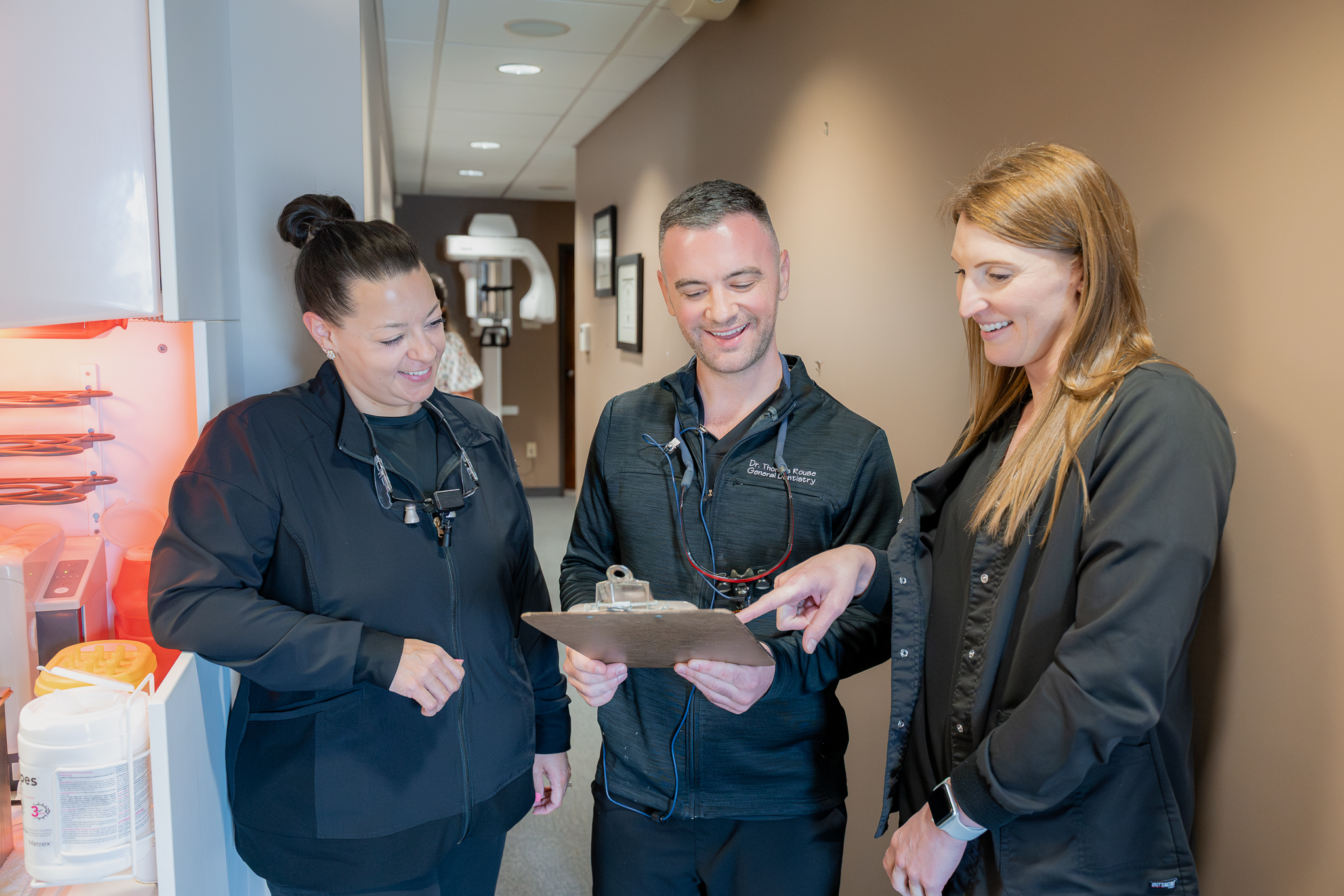 Dentist reviewing a clipboard with two team members in the hallway