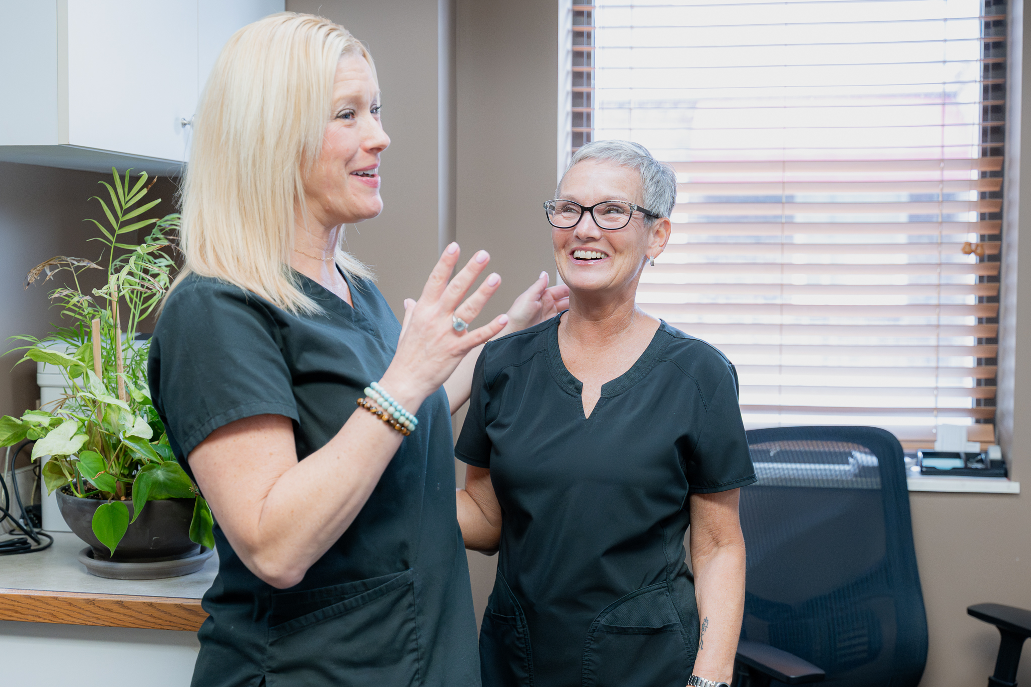 Two team members in black scrubs laughing together in the office