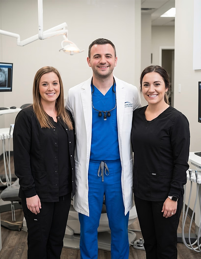 Smiling dentist in a white coat with two dental team members in a treatment room